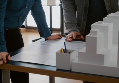Close up of colleagues working on urban design with blueprints and building model. Team of people doing teamwork on construction layout, designing architectural development project