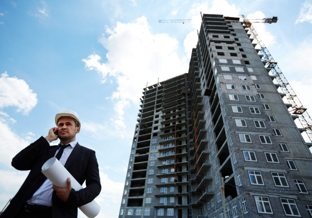Elegant investor in helmet talking on mobile phone by unfinished building